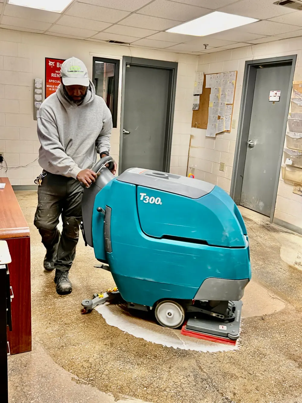 Crew member running a walk-behind floor scrubber down a building hallway