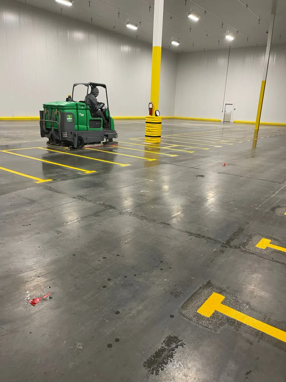 Ride-on floor scrubber on a gray concrete floor with yellow safety markings