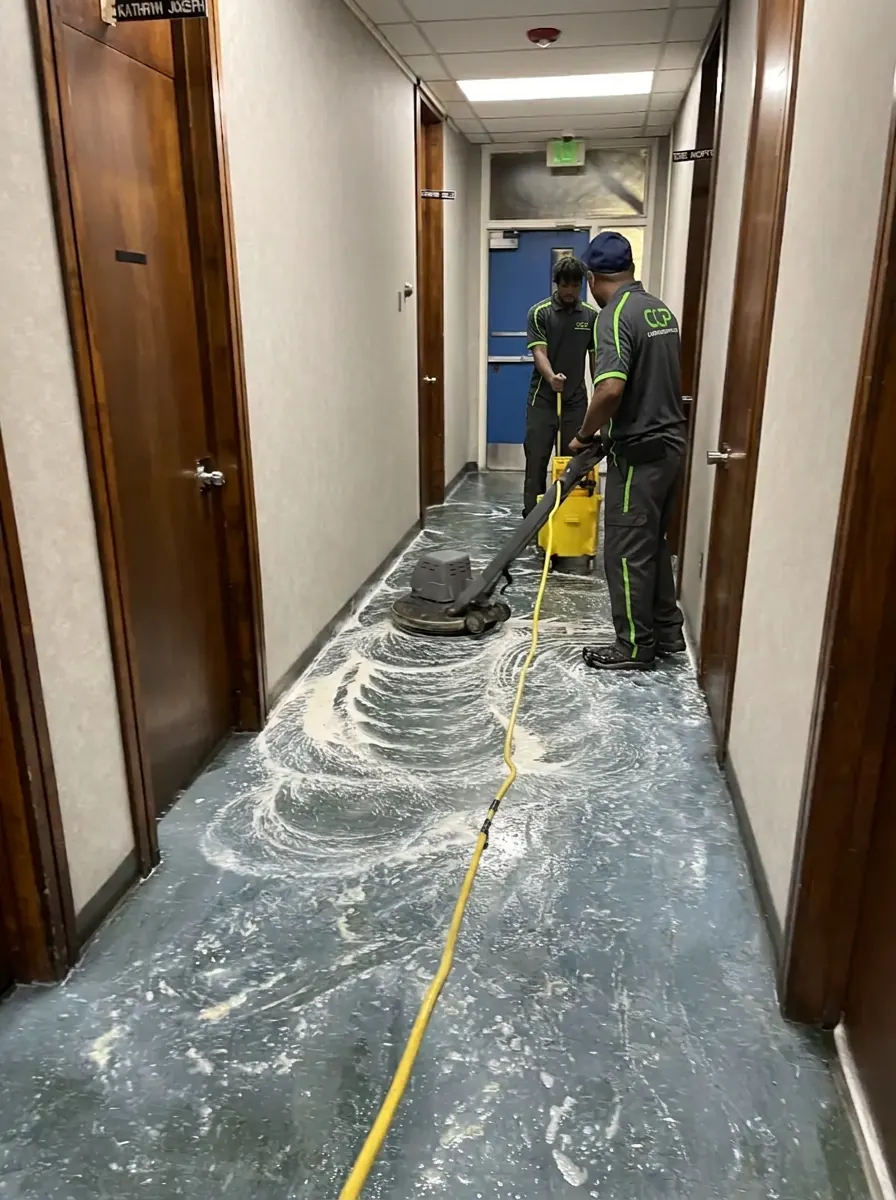 Two crew members stripping old floor finish in a hallway with a buffing machine