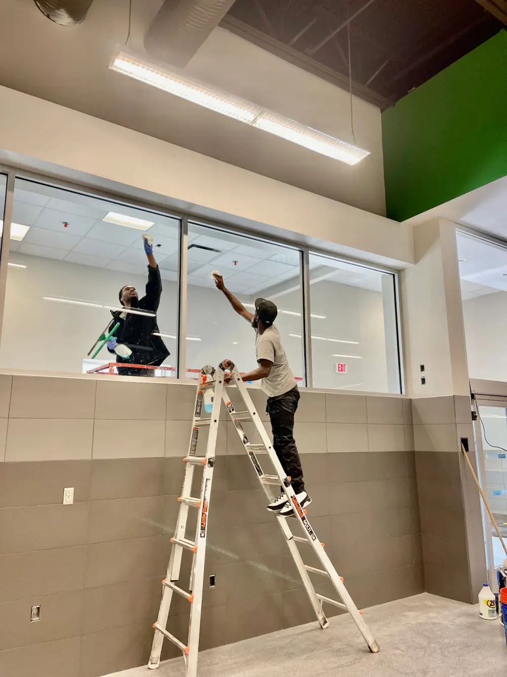 Crew member on a ladder cleaning interior glass above a wall