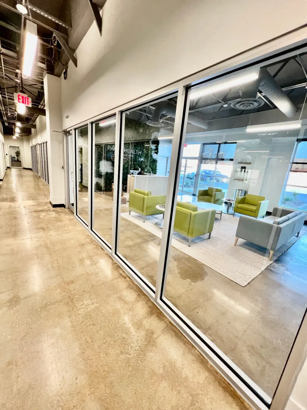 Freshly cleaned office corridor beside a glass-walled lounge with green chairs