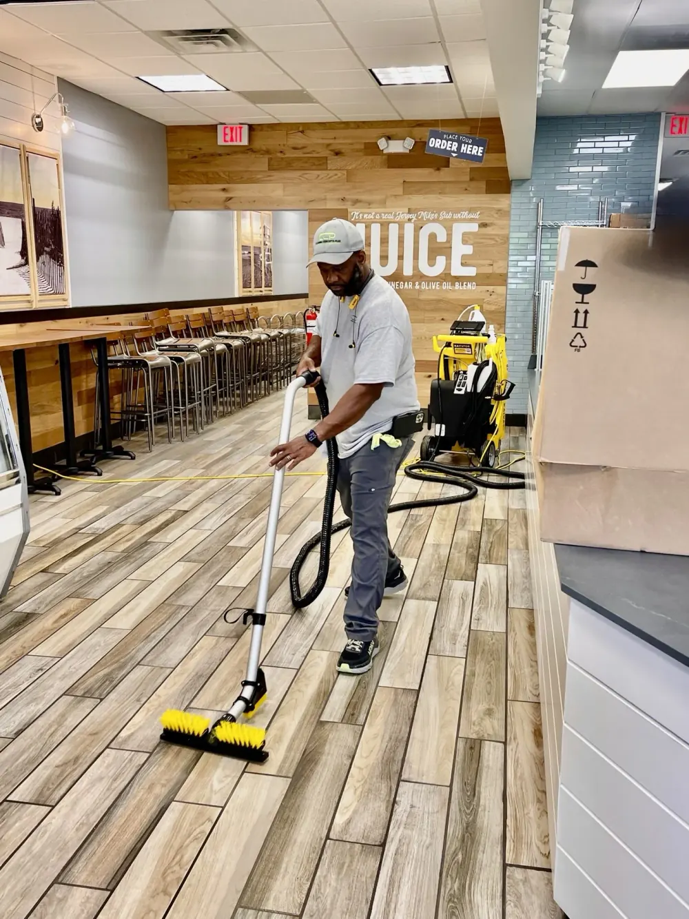 Crew member vacuuming a wood-look tile floor in a food service dining area